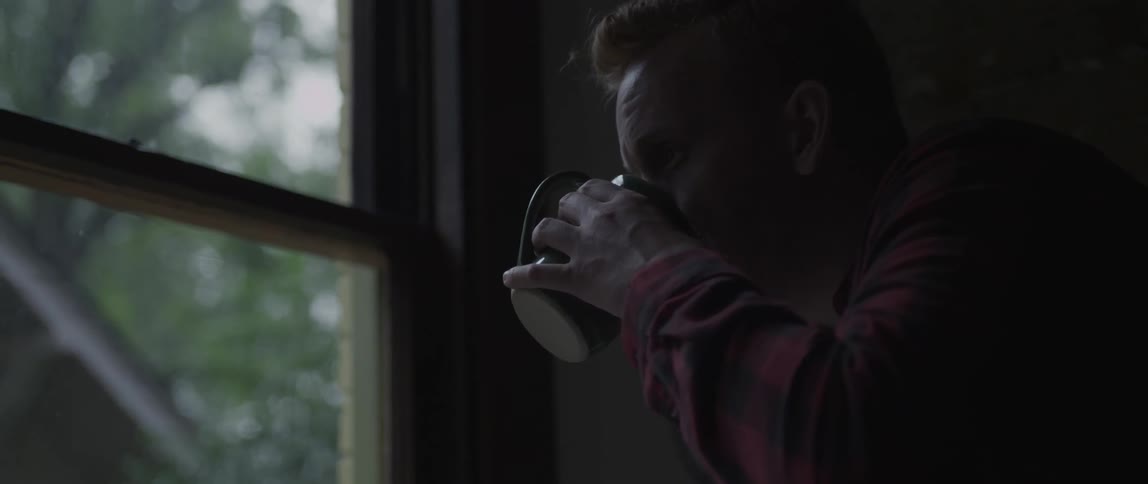 A man drinks from his mug while watching the rain