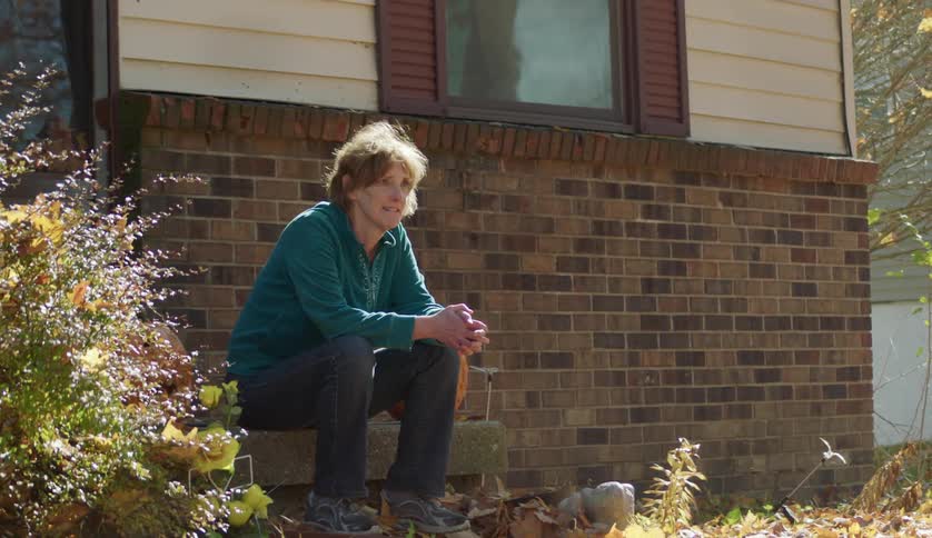 An older woman is sitting down on a bench outside