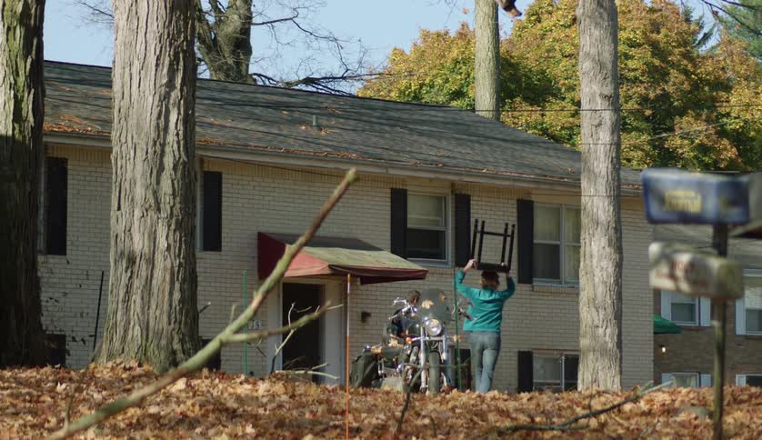 A man and a woman are carrying a mattress and table into a building with a motorcycle parked in front