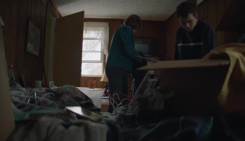 Woman and young man work to clean cluttered wood paneled room