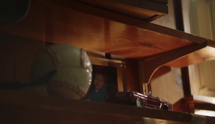 Photograph of child sits on wooden shelf next to baseball and toy car