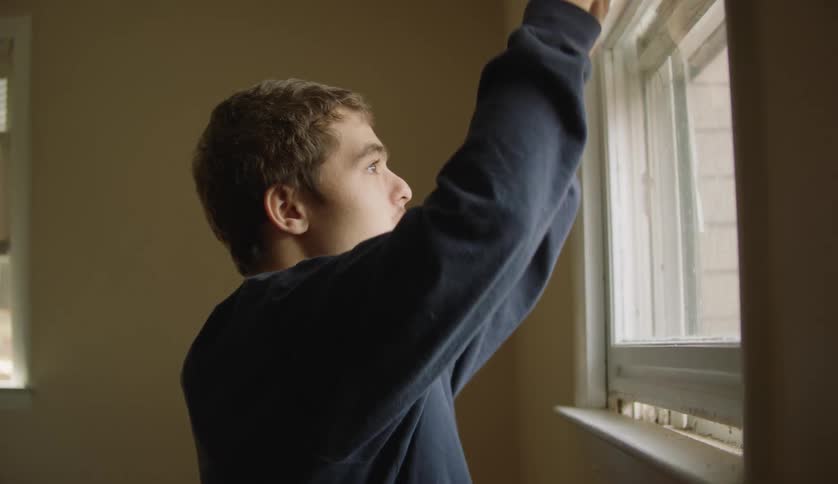 Male lifting up white blinds from a bedroom window