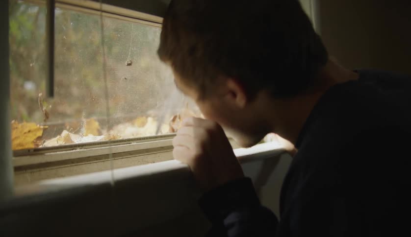Male looking out a closed windows indoors and looking around