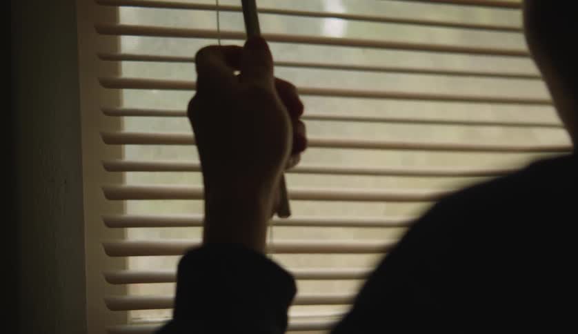 Silhouette of a person opening the shades on a window
