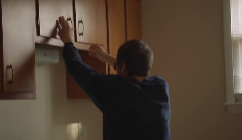 A young man opening and slamming kitchen cabinets shut
