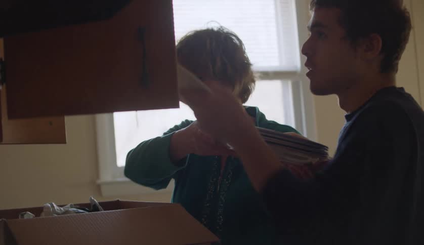 A grandmother and her grandson are putting dishes into a cabinet