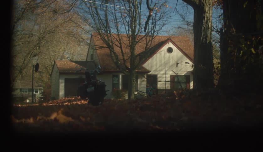 A person raking autumn leaves in front of their house in a residential area