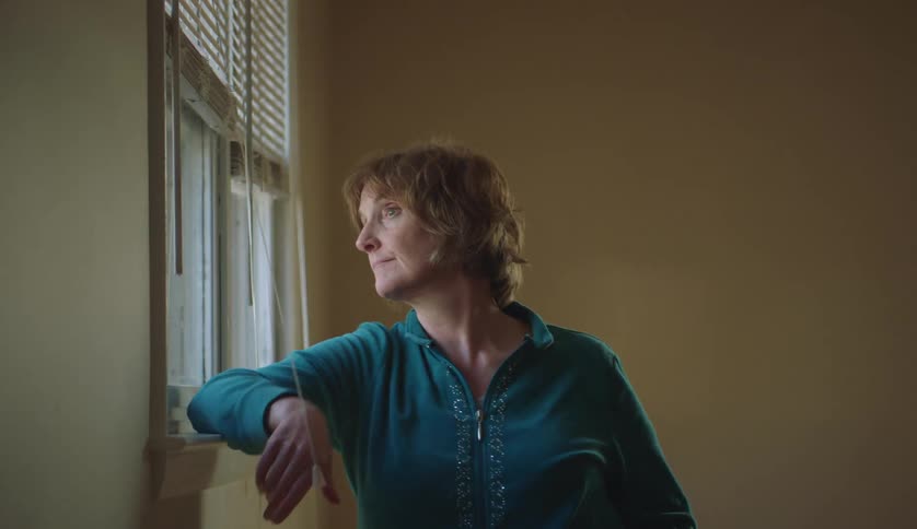 A woman is looking out a window while standing indoors