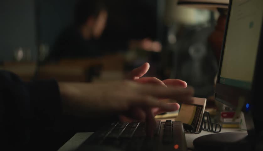 A person rapidly taps a key on their computer keyboard while sitting at a desk