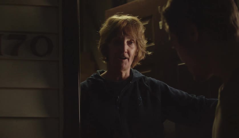 Middle aged woman with brown hair and zip up hoodie talks to man at the door
