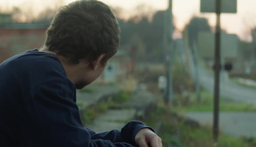 A male is sitting outdoors while the sun is setting