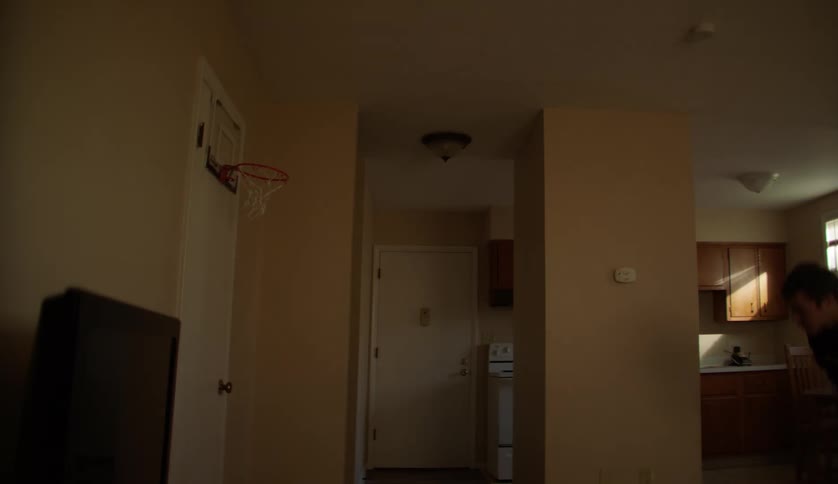 A teenage boy is shooting baskets with a small ball and a hoop on the back of a door