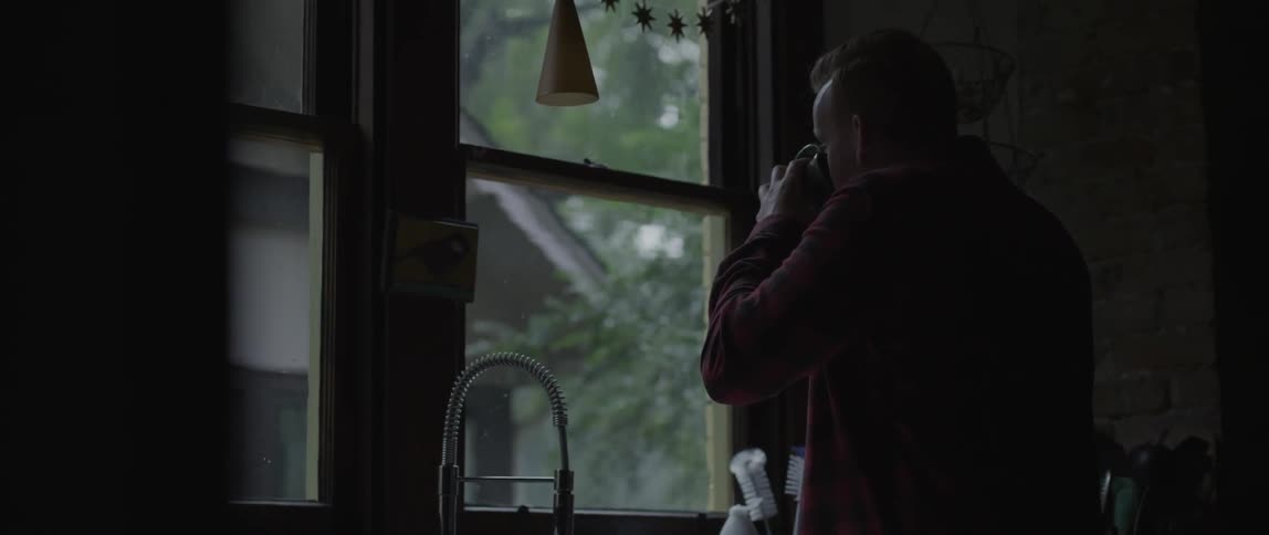 A man drinks from his mug in front of a window