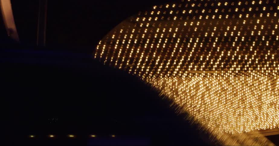 A vehicle drives past a downtown building with a brightly lit awning