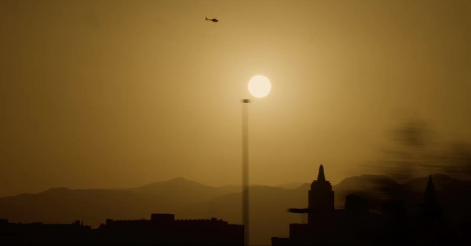 Silhouette of a helicopter flying over the sun setting on the city skyline
