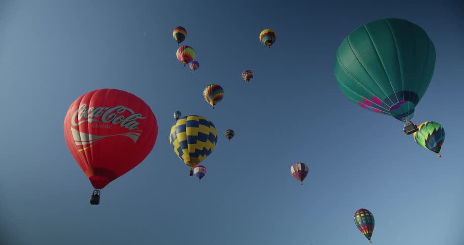 The sun shines on colorful hot air balloons as they float in a clear blue sky