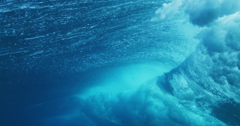 Underwater view of a wave rolling overhead and sunlight reflecting the ripples as water splashes