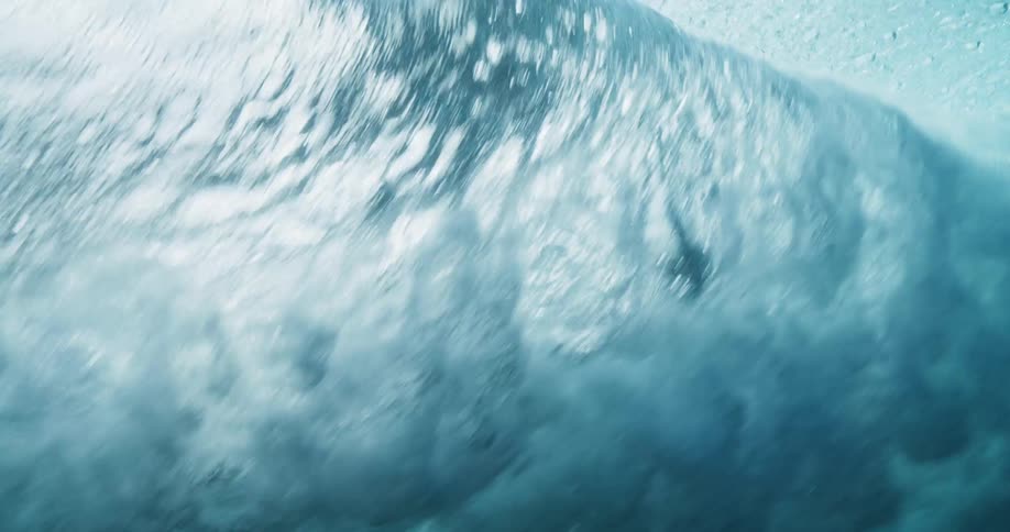 Underwater view of a wave rolling overhead and sunlight reflecting the ripples as water splashes