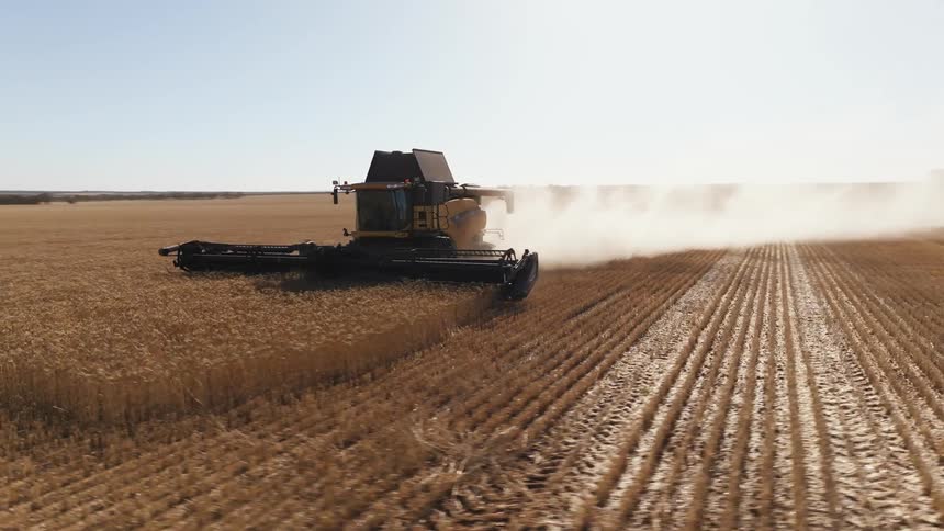 A tractor is plowing a field on a farm and leaving behind a cloud of smoke