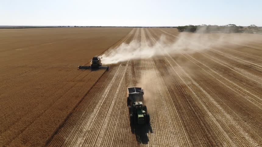 Tractors on a farm are plowing a field and leaving a trail of smoke