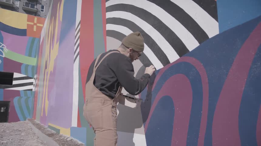 An artist touching up a painted mural on an outdoor wall