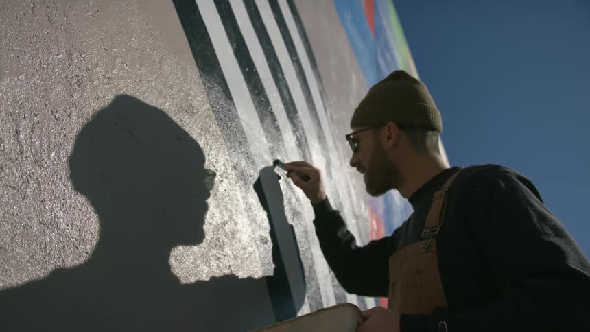 A man is standing outside painting a design on the wall of a building