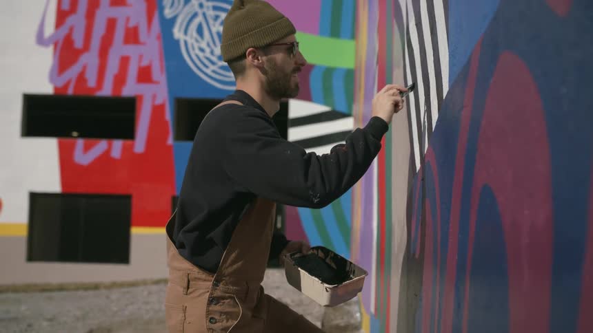 A man is standing outside painting a design on the wall of a building