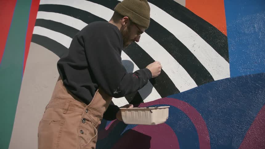 A man is standing outside painting a design on the wall of a building