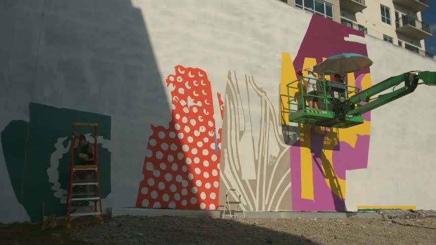 Time lapse of people using a crane to paint a mural on a wall outdoors