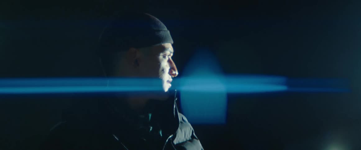 A man bundled in a puffer coat and hat stands in a parking lot