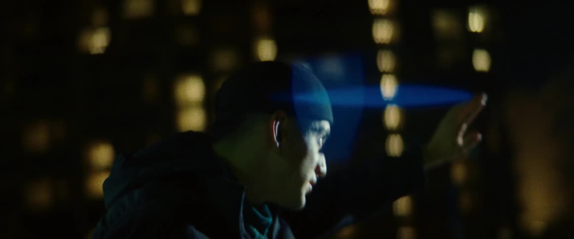 Young man standing in the city at night shields his eyes from a bright light