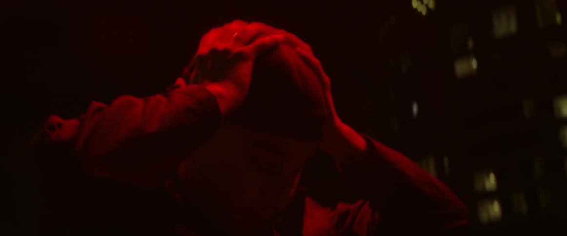 Red colored lights shine on man as he puts hands to head outdoors at night