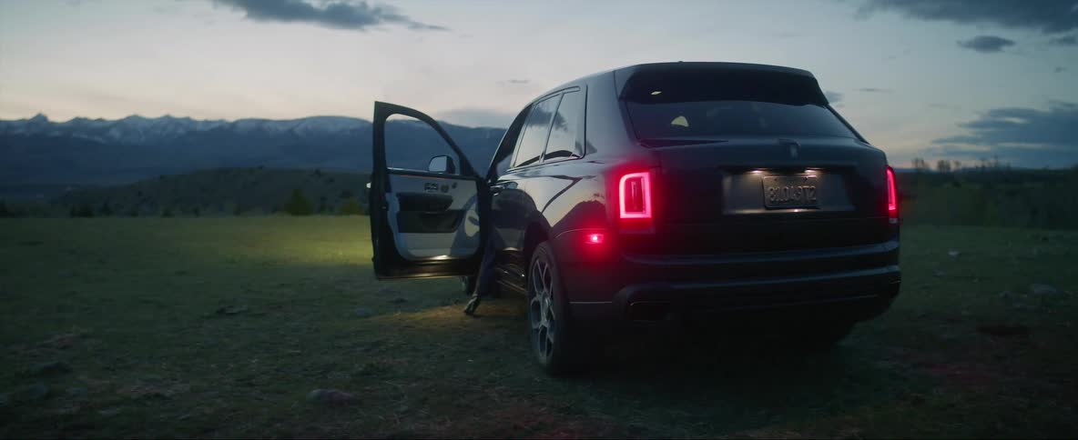 Two people dressed like wild west characters board a car parked on a field at evening