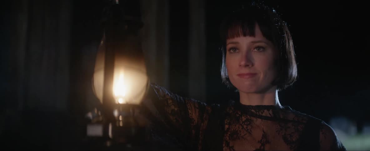 A woman holds a lantern up while she stands in the darkness while looking uncertain