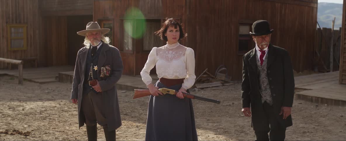Wild west woman holds a rifle on her hands next to two deputies in town