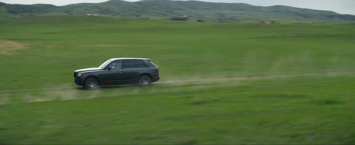 Cowboys riding horses follow a car driving on the plains at daytime