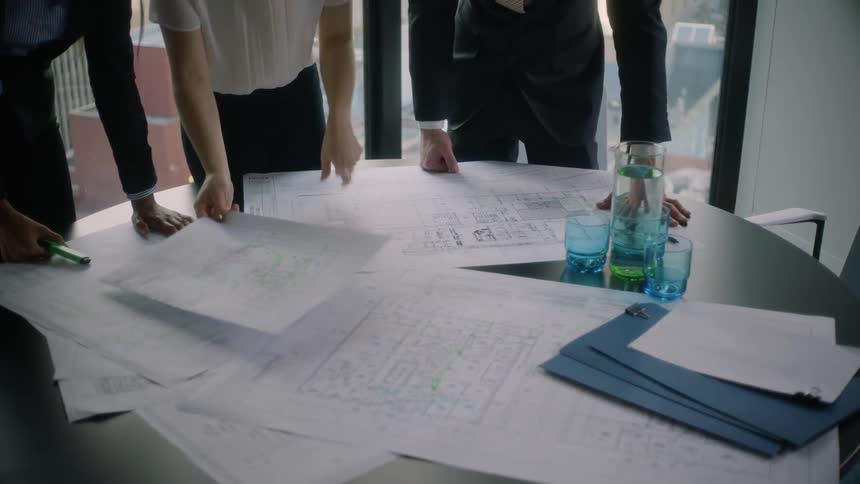 Three people look over blueprints on a table