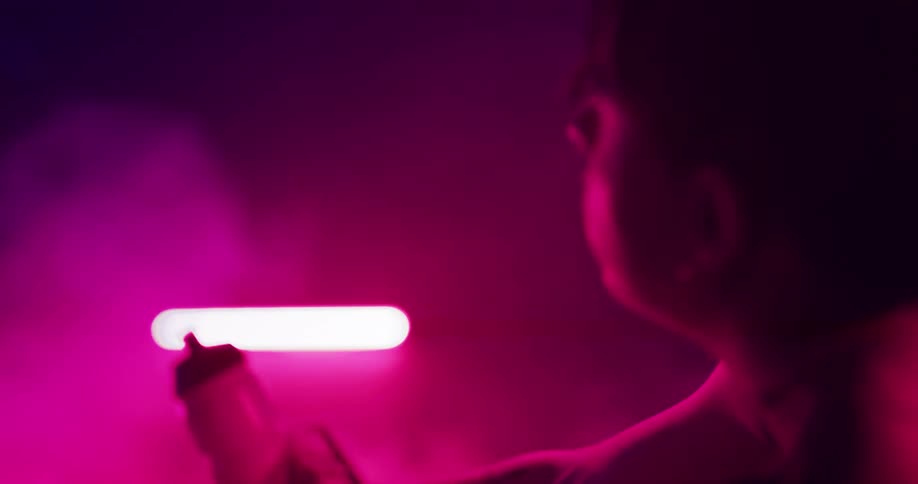 Young woman pedaling on a static bycicle drinks water on a room filled with smoke and magenta lights