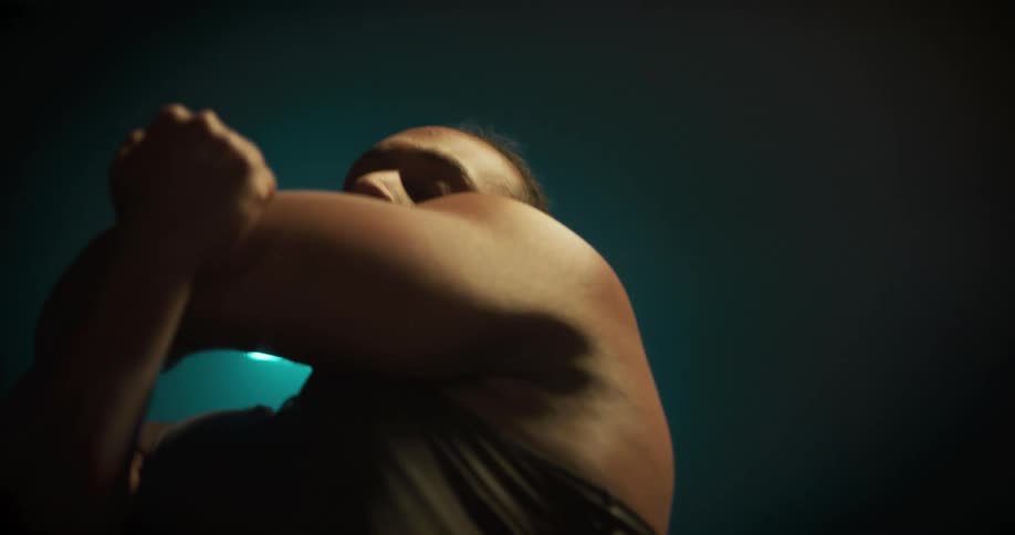 A muscular man stretches his arms in a dimly lit room