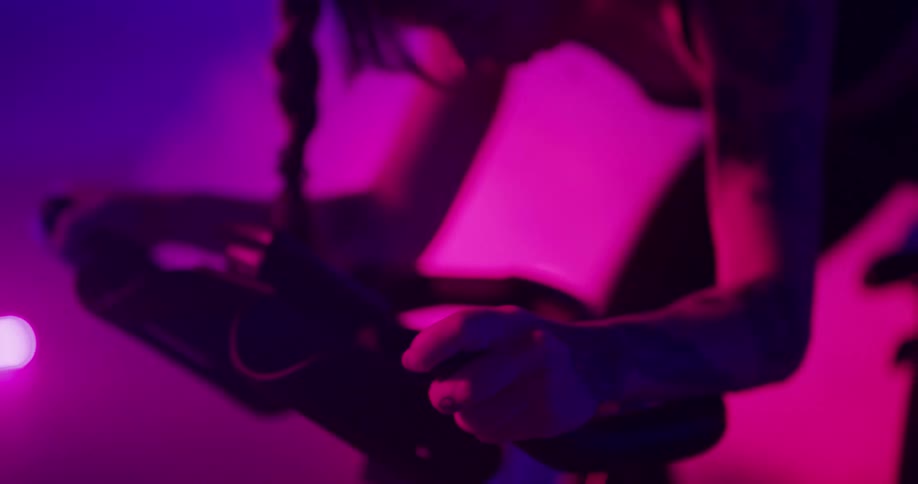 Woman pedals rapidly on stationary bike in room lit by colored lighting as smoke spreads in the background