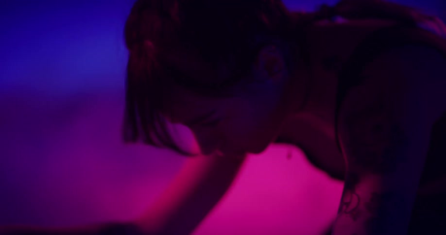 A woman is pedaling an exercise bike and there are pink and purple lights in the distance