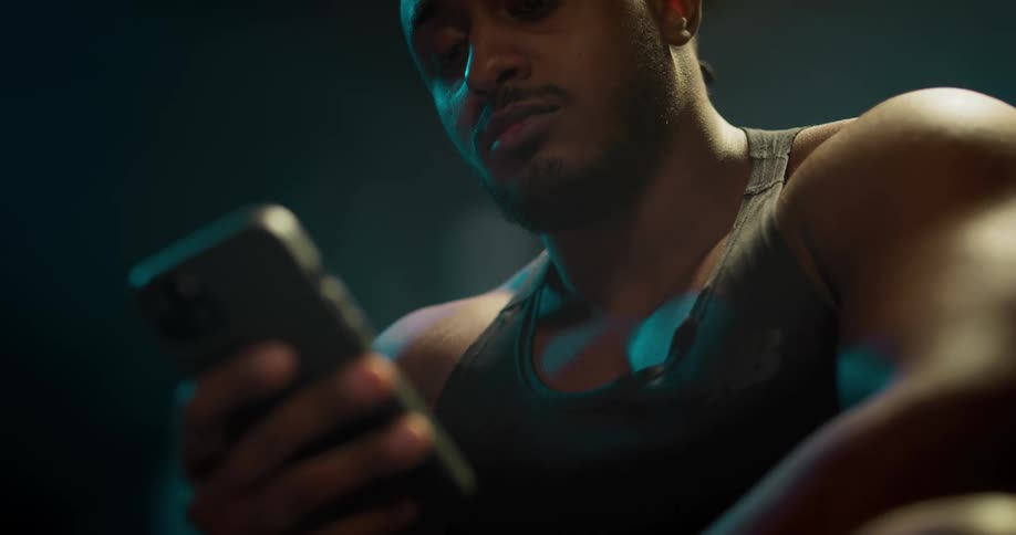 A man is sitting down holding his cell phone and looking at it