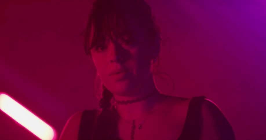 Woman scrolling on smartphone in room lit by colored lighting looks up to stare