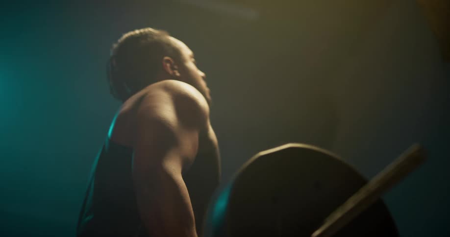 Light shines on a man as he is working out weight lifting with a barbell