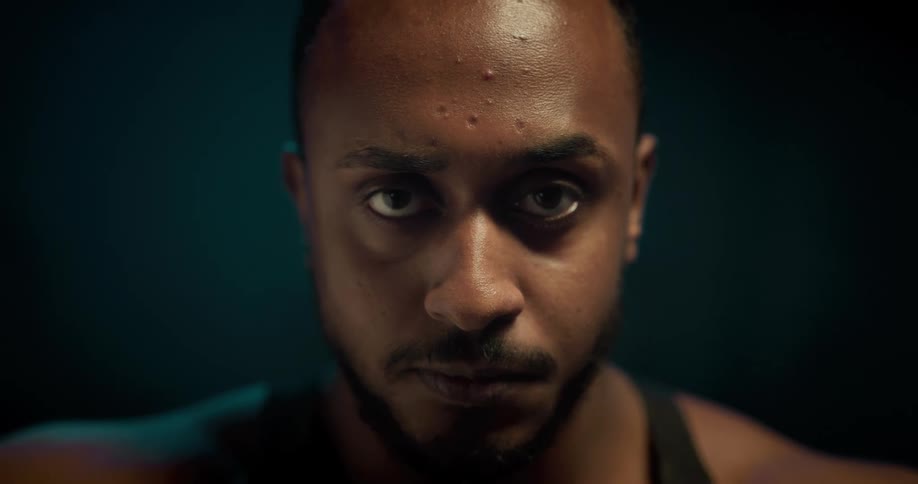 A man lowers his head and licks his lips while staring into the camera