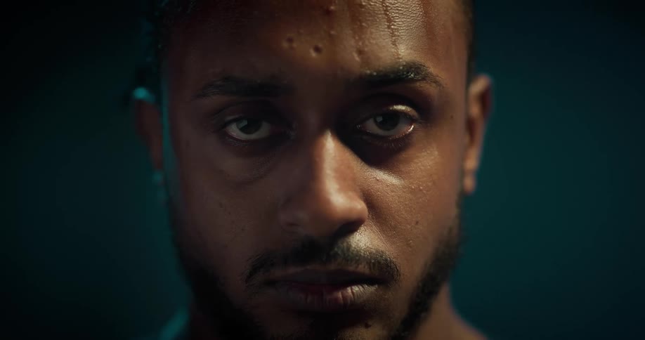 A sweating man stares into the camera with a serious expression on his face
