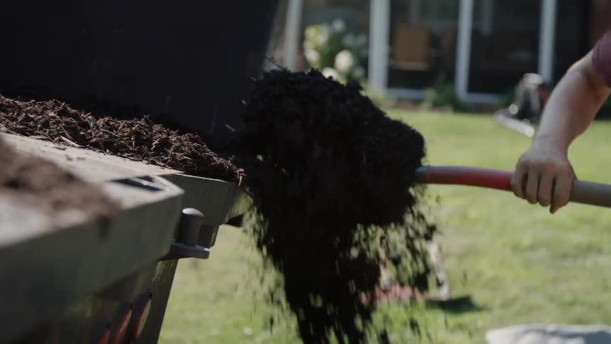A man scooping compost from the back of a truck bed
