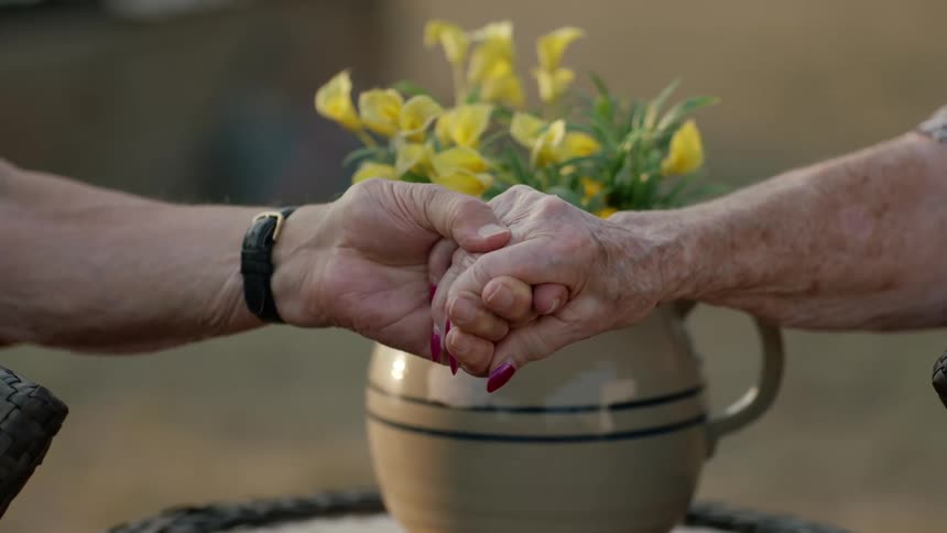 Elderly couple hold hands in front of a vase filled with yellow flowers