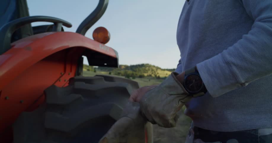 A man puts on working gloves before getting on his tractor