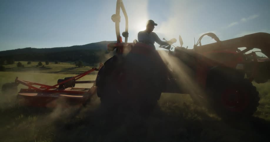 A tractor is plowing a field on a farm as the sun shines brightly in the distance